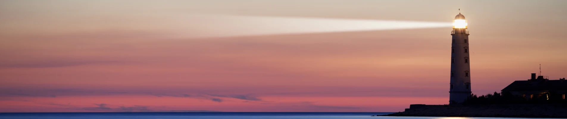 Lighthouse shining a beam of light over the ocean at sunset or sunrise with a pink and purple sky