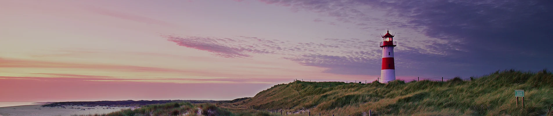 Red and white striped lighthouse on sand dunes of Sylt island, Germany, at sunset